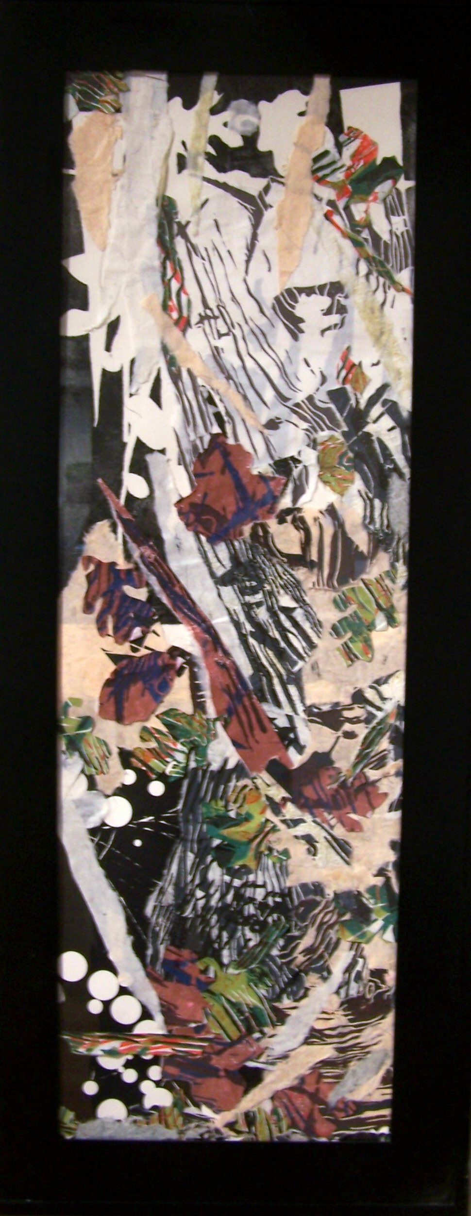 This collage is a non-representational piece. It is a tall vertical work that is probably four times taller than it is wide. It consists of many pieces of paper that are torn or cut into organic shapes. Some of the papers are tissue-like and some appear to be black and white  organically stripped or dotted prints along with other papers that had a texture or print on them. The papers are white and black, cream, red with blue and black marks, and green with teal and orange marks. It has a flow that begins from the upper left and moves down the work towards the bottom right.