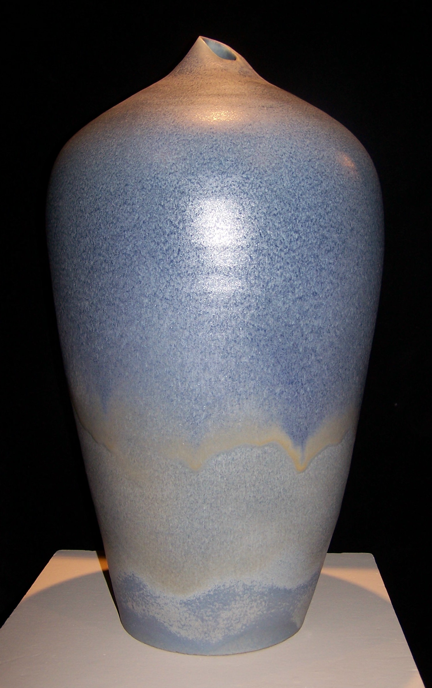 Despite the title of the work, this tall ceramic vase is not a traditional amphora shape. Narrower at the bottom, it flares out towards the top but comes back in sharply and has a very small opening at the top. The opening is asymmetrically cut on a diagonal.