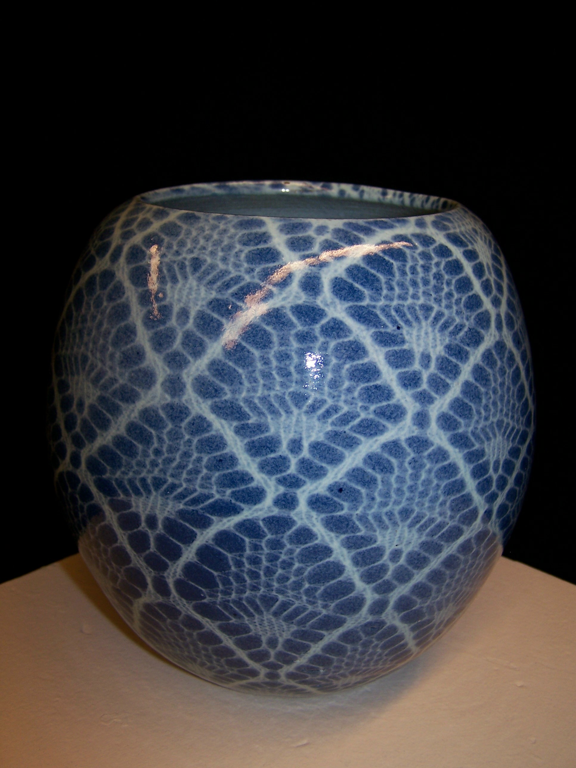 A nearly spherical vase with a lace pattern on it in white with a blue background.