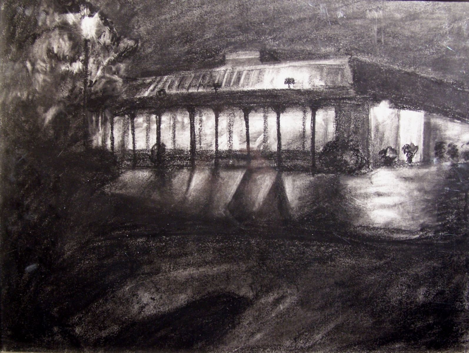 A charcoal drawing of a two-point perspective building at night. The windows are illuminated from the inside. The building has repeating thin columns on one of its sides and the interior light illuminates the ground outside. The bottom half of the work is shadow shapes. The left side of the work has non-distinct greenery and a bright streetlamp in the middle ground. There are some smaller planters and greenery in shadow around the building.