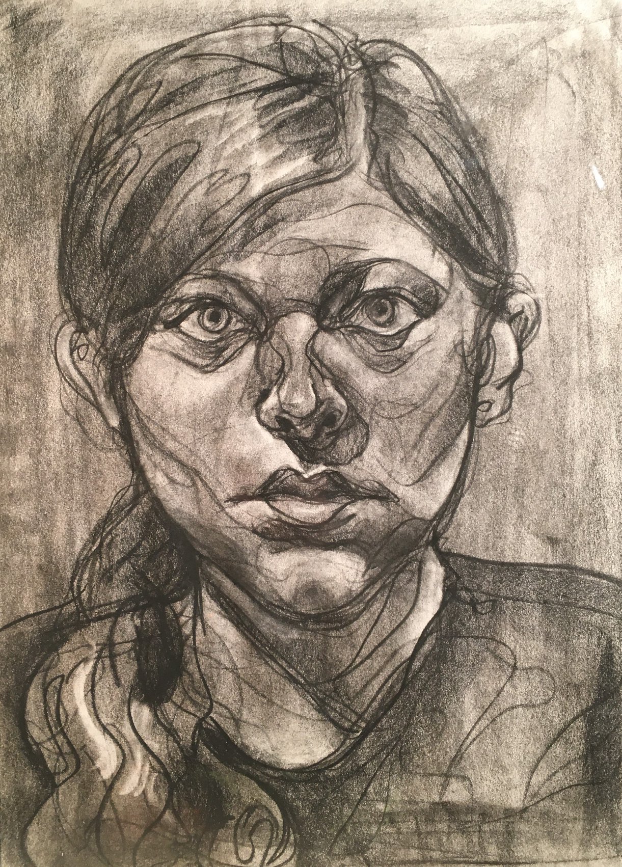 A charcoal portrait of a young woman. She stares directly out at the viewer. Her hair is pulled back, but the low ponytail comes forwards on her right shoulder. There is both value and line describing her form. The lines are loose, very active, somewhat sparse, but stay within the figure.
