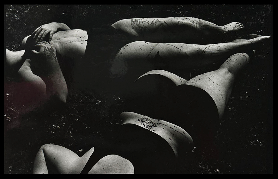 "Dahlia and Dahlia" by Joan Galbraith: A Black and White photograph featuring two female figures lying on the ground in dark swimsuits or underwear with their bodies ominously splattered with dark liquid. The top figure is laying mostly parallel to the top of the frame with her hands on her chest and the bottom figure is laying face-down diagonally towards the bottom left of the frame with her legs underneath to the other figures legs. Both faces are cropped out of the photograph.