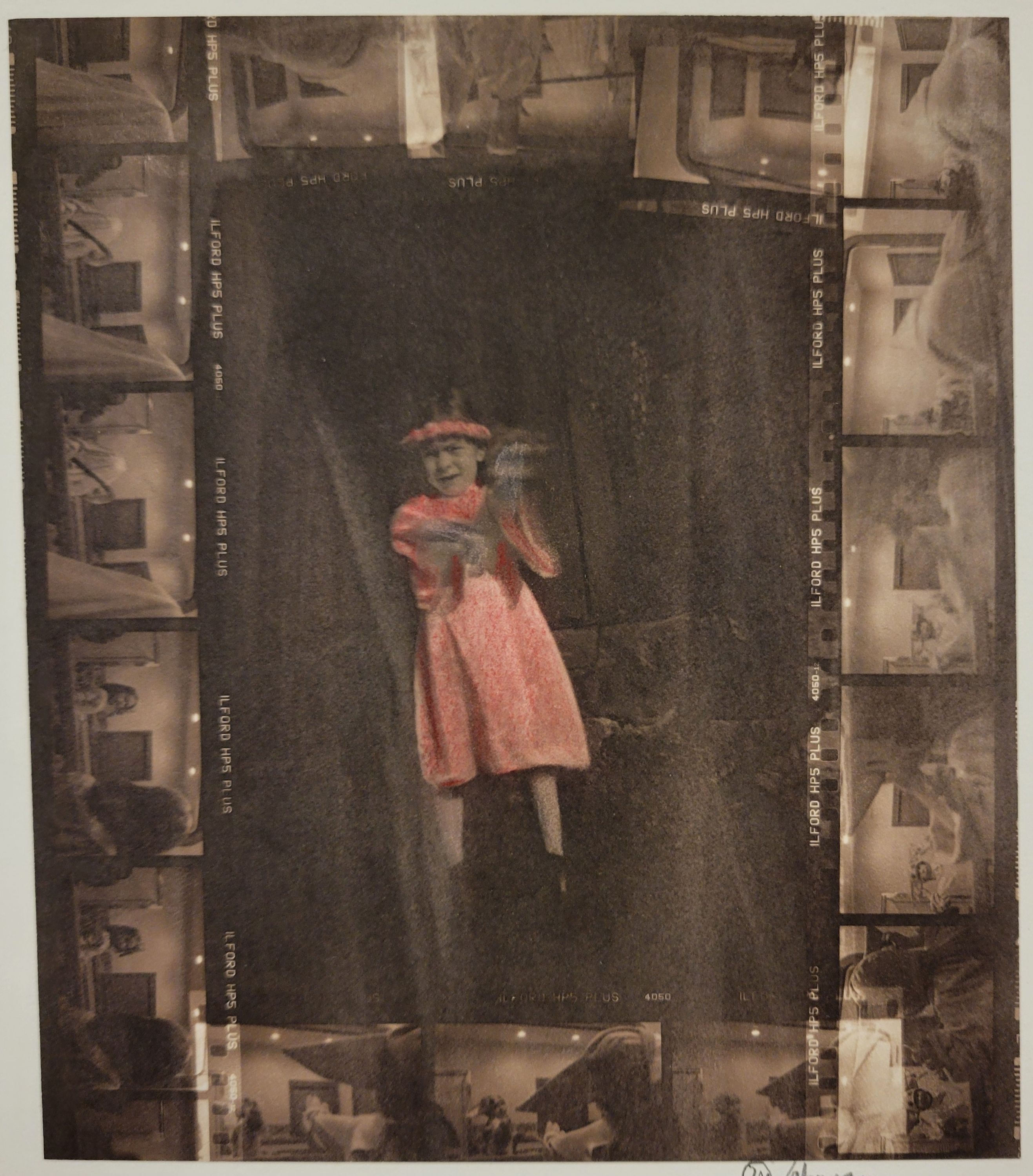 A hand colored contact print. The center of the image is a young girl, whose dress has been hand colored red. She also has a red headband that she is wearing that matches the dress. She stands out against the dark background. Surrounding the image of the girl is four strips of film. These strips are also depicting a girl but now in front of a mirror. She is trying on different looks, one of her in the dress, on of her in a bonnet, and one of her in a blanket like a ghost.